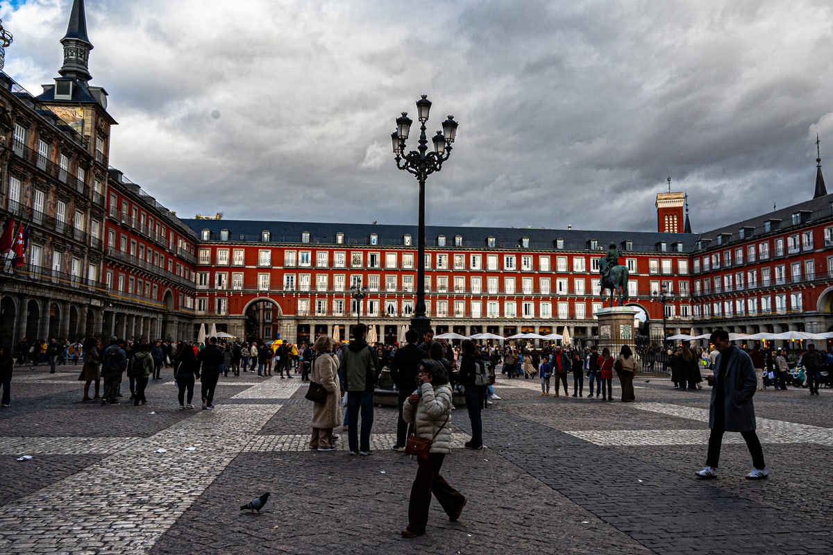 Storm clouds over Plaza Mayor in Madrid as people cross the cobblestones.