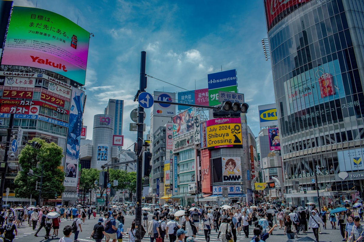 Crowds pour across Shibuya Crossing in Tokyo beneath giant billboards.