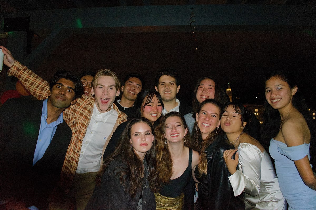 A big group of friends crowds together laughing on a rooftop at night.