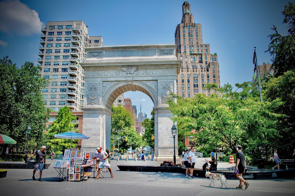 The Washington Square Arch on a bright summer day with people walking past.