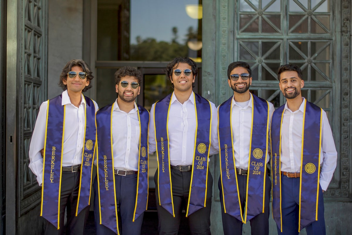 Five graduates in sunglasses and Class of 2024 stoles stand shoulder to shoulder in an ornate doorway.