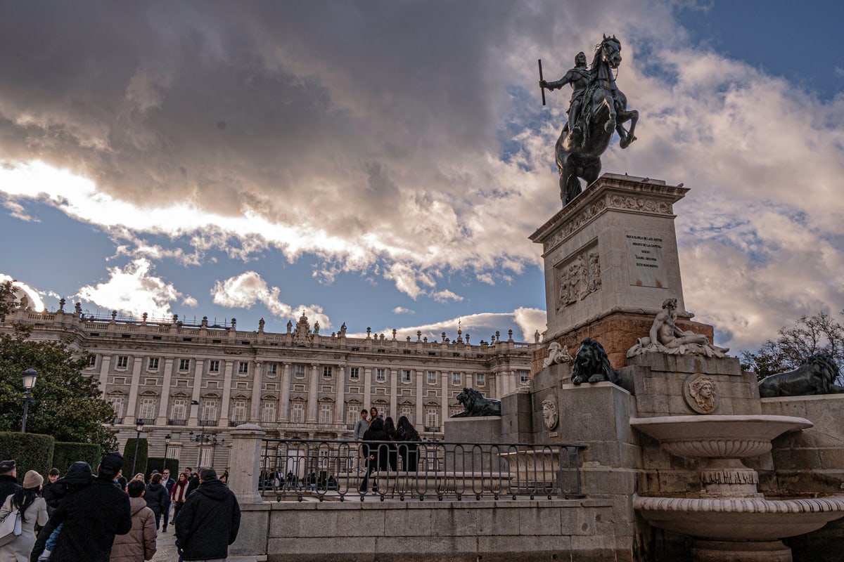 An equestrian statue in front of the Royal Palace of Madrid under dramatic clouds.