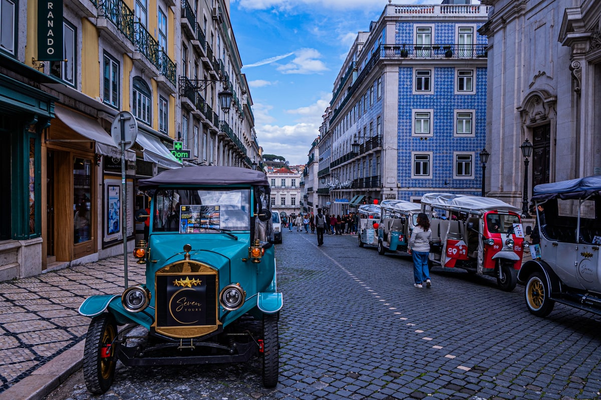 A vintage blue car waits on a cobblestone street lined with tiled buildings in Lisbon.