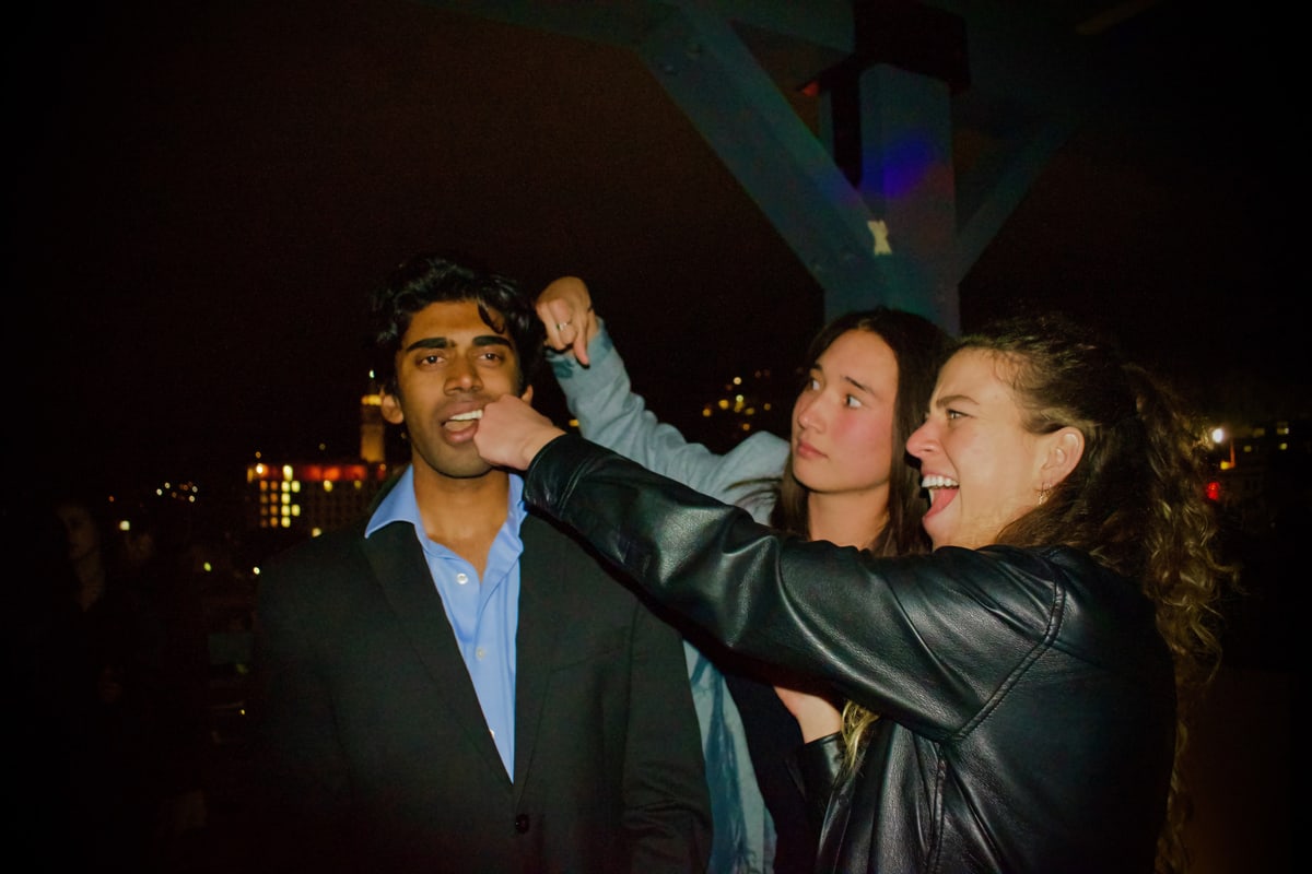 Two friends tease a man in a suit, pinching his cheek and laughing.
