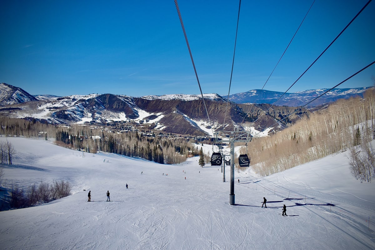 A gondola line runs down a wide ski slope toward the valley.