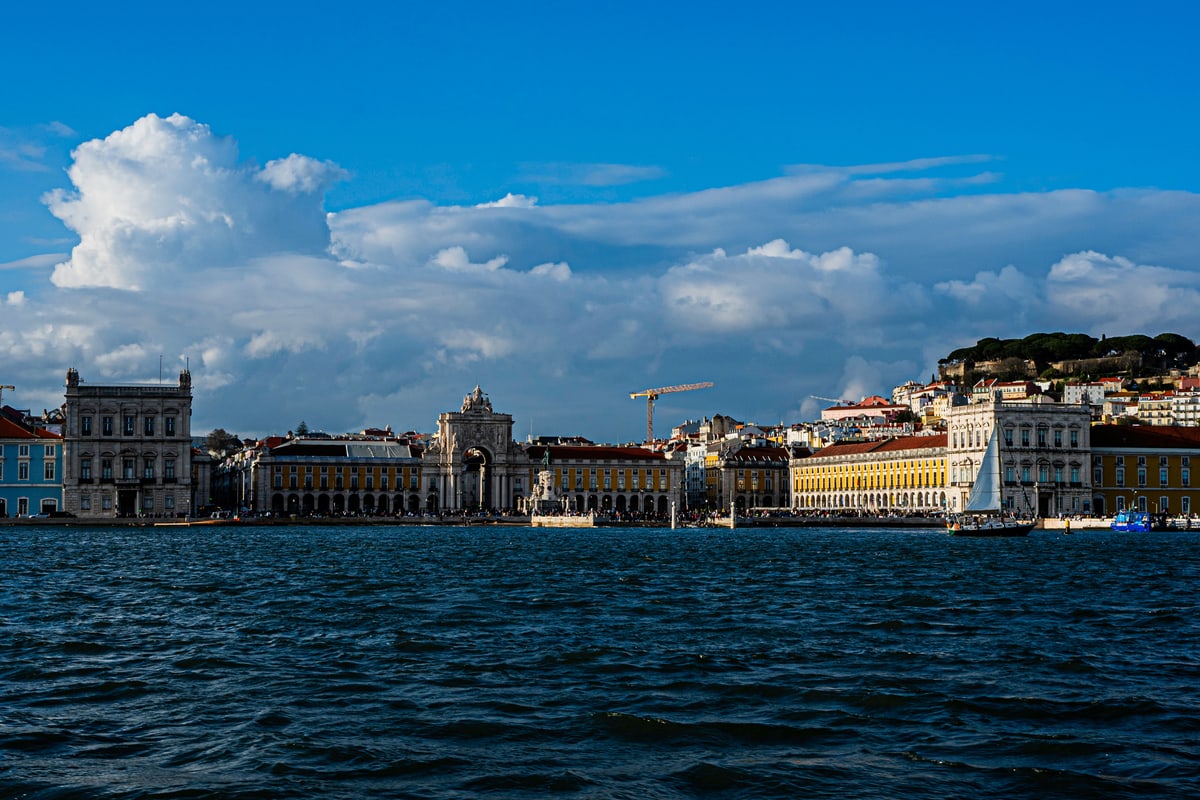 Lisbon's waterfront and hills seen from the Tagus River under big clouds.