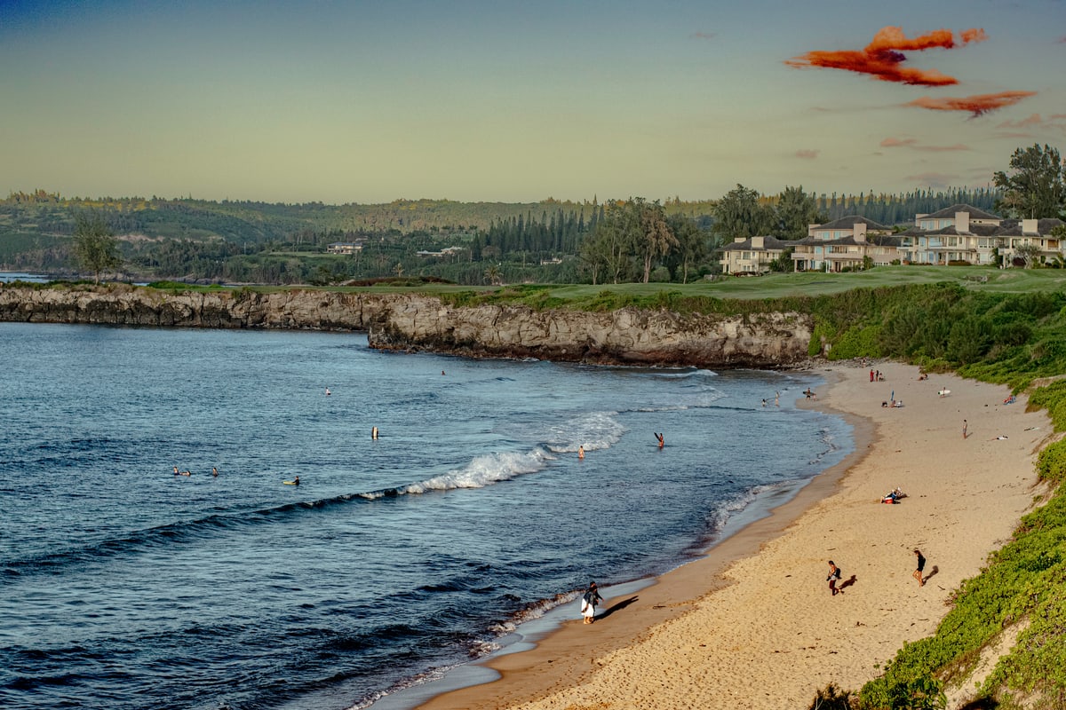 Waves roll onto a golden beach beneath green cliffs.