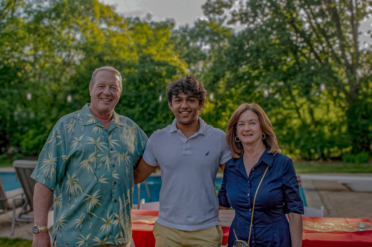 A smiling graduate stands between two family friends at a backyard party.