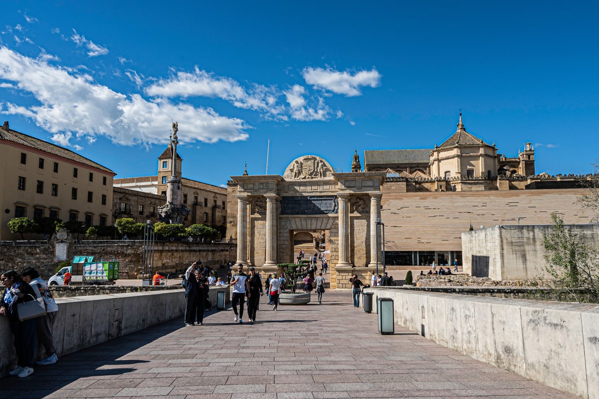 A wide stone walkway leading to an old city gate in Córdoba under a blue sky.