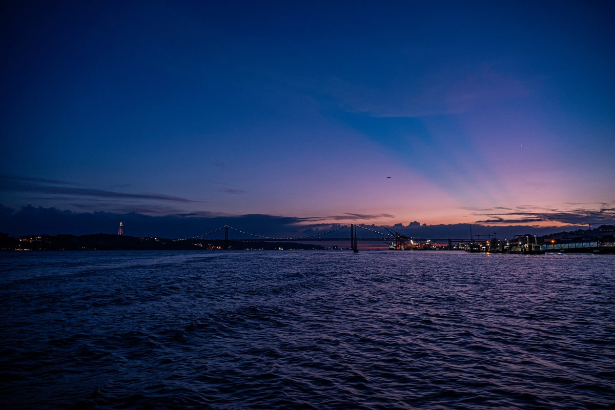Purple dusk over the Tagus River, the 25 de Abril Bridge faint on the horizon.