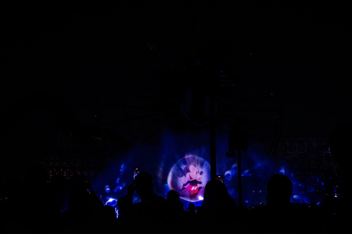 Silhouetted crowds watch a glowing water show at night.