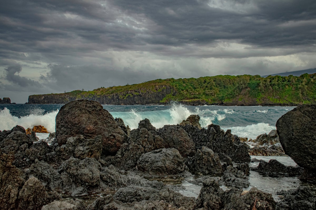 Waves crash over black lava rocks under a heavy grey sky.