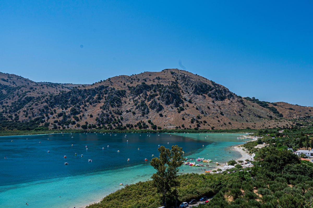 A turquoise bay with boats anchored below green mountains.