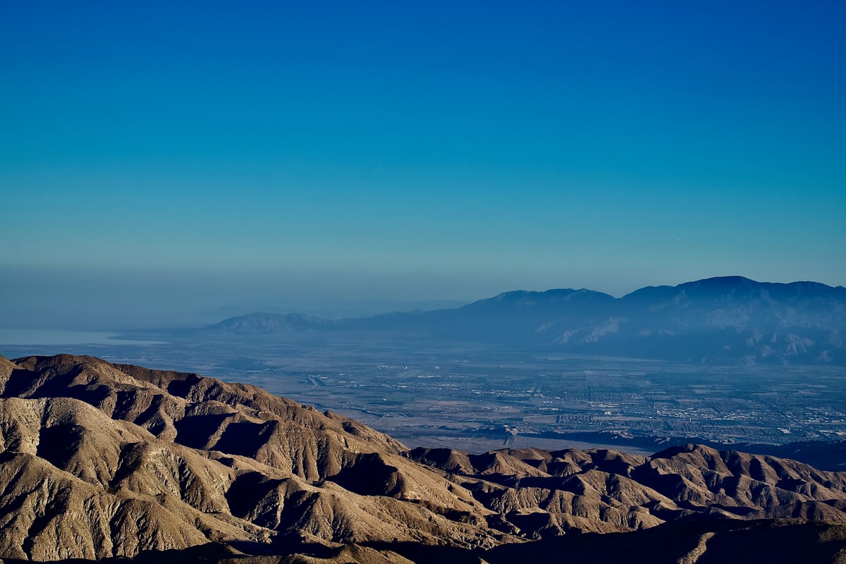 Eroded desert badlands roll toward distant mountains under a blue sky.