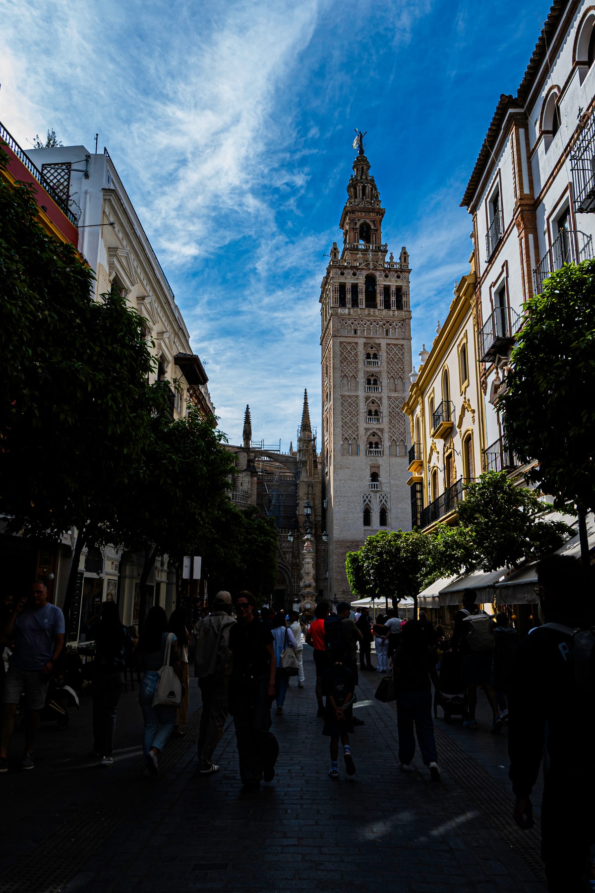 The Giralda bell tower rises at the end of a shaded street in Seville.