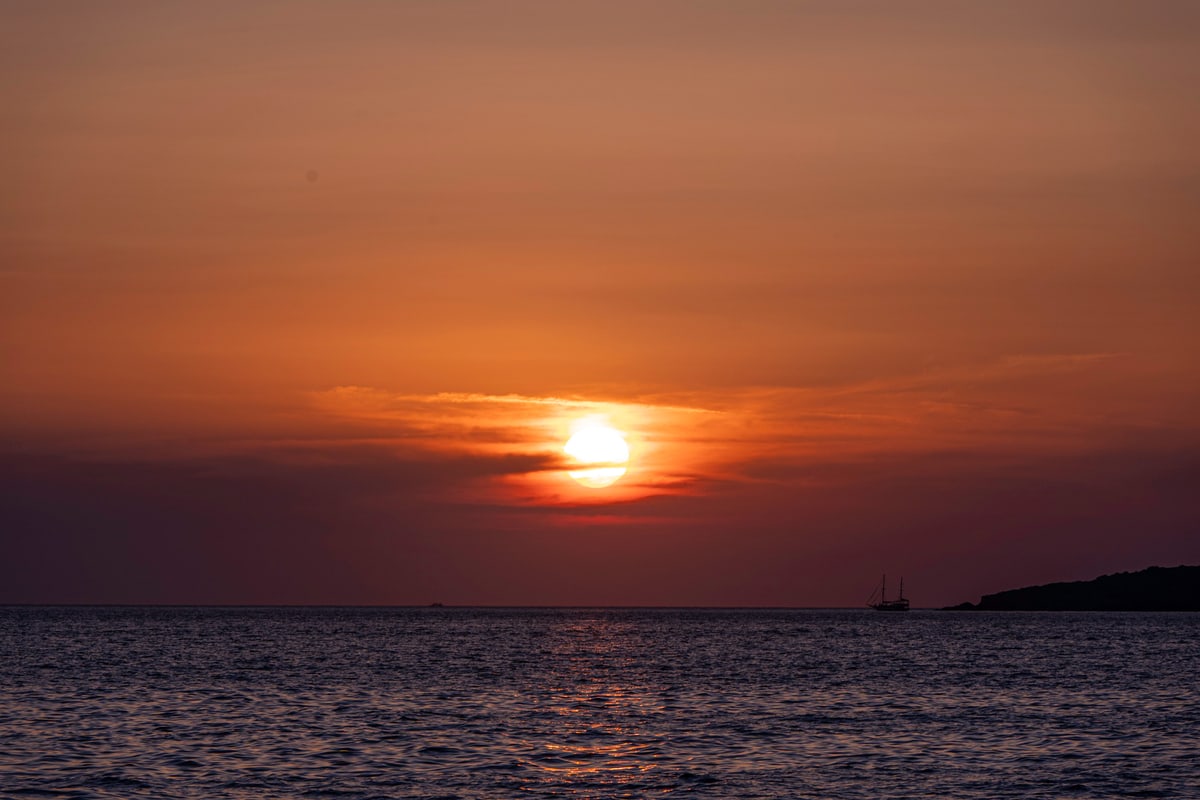 The sun sets behind thin clouds over the Aegean Sea.
