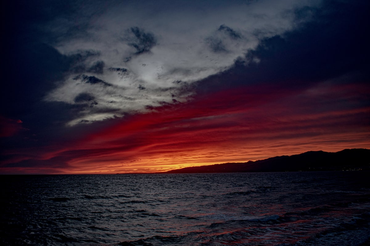 A dramatic sunset glows red beneath dark clouds over the Pacific.