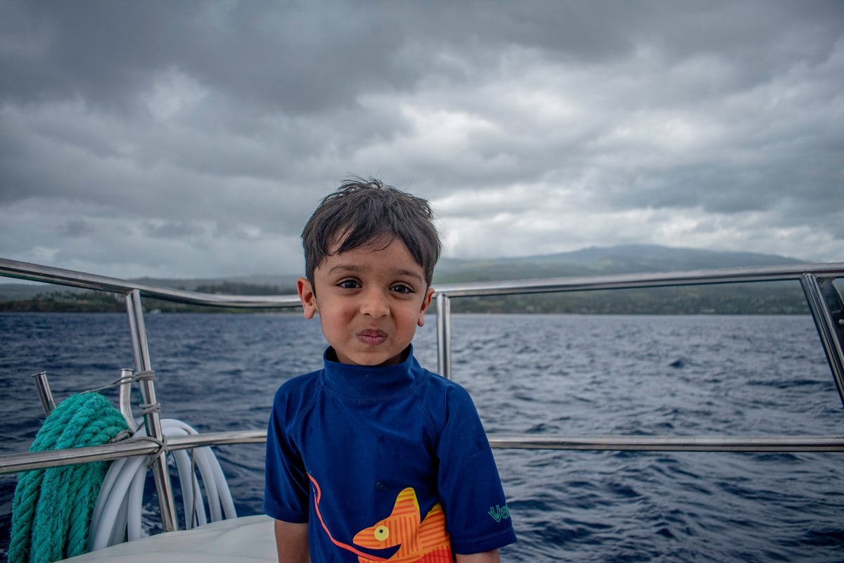 A young boy smiles on a boat under dramatic storm clouds.