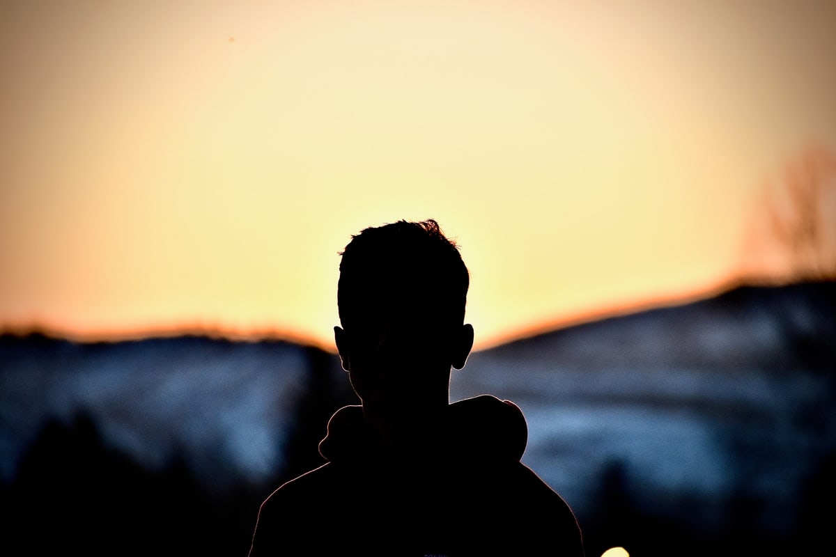 A child's silhouette against a golden sunset over the hills.